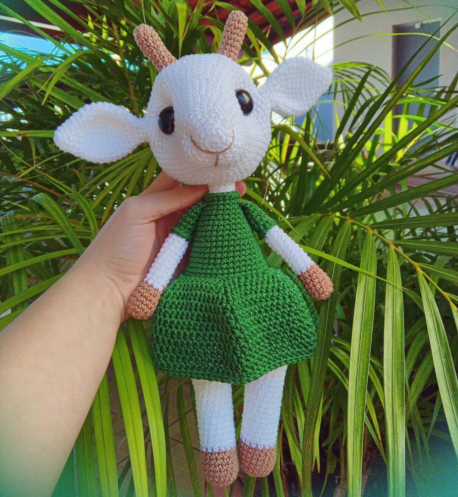 Foto de um amigurumi de uma cabra branca vestindo um vestido verde escuro