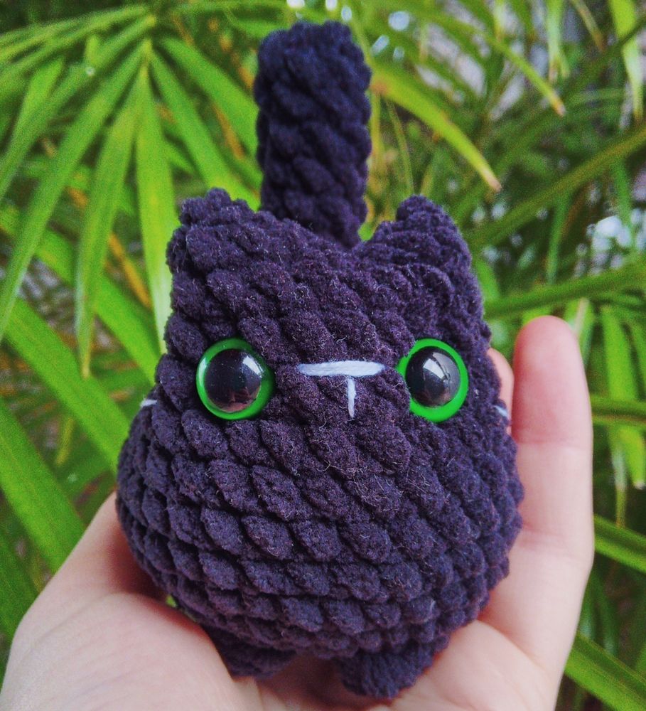 Foto de um amigurumi de um gato preto de olhos verdes visto de frente
