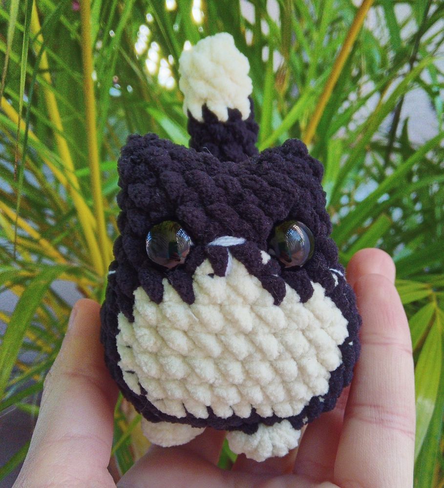 Foto de amigurumi de um gatinho preto com as patas, barriga e ponta do rabo brancas visto de frente 