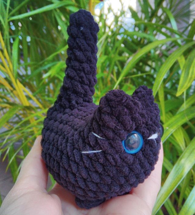 Foto de um amigurumi de gato preto visto de perfil mostrando seu olho azul e bigodes brancos 