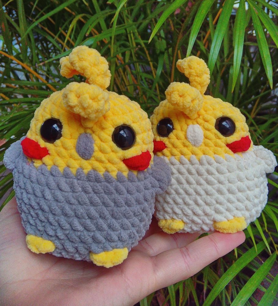 Foto de dois amigurumis de calopsita. A da esquerda é cinza com amarelo e a da direita é amarelo com branco 