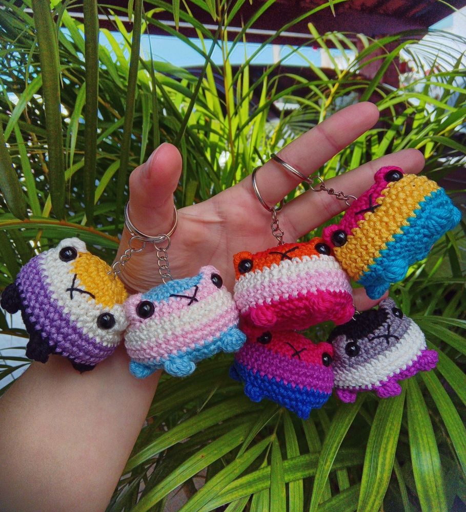 Foto de seis chaveiros de amigurumis de sapinhos e cada um tem uma bandeira. Tem não binário, trans, lésbica, pan, bi e assexual 