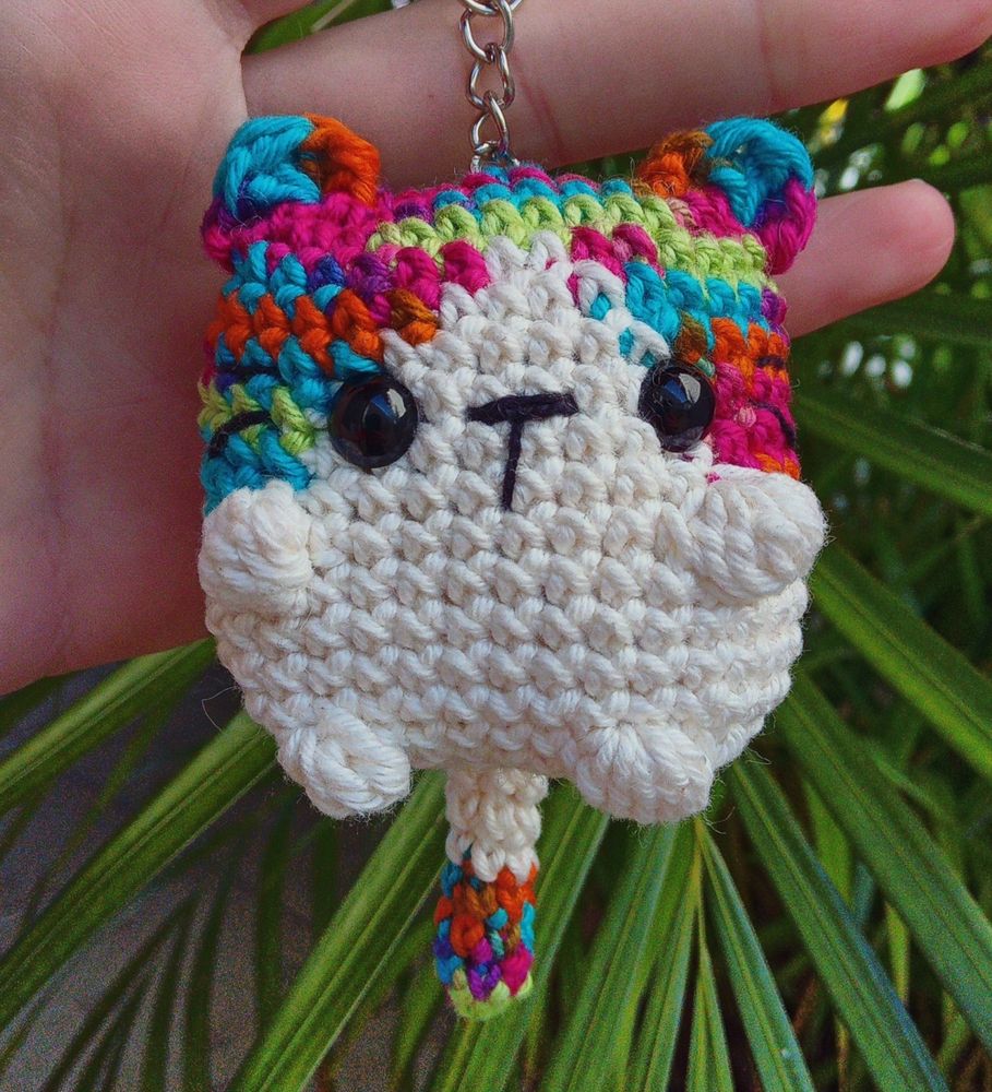 Foto de um amigurumi de um gatinho branco com detalhes coloridos 