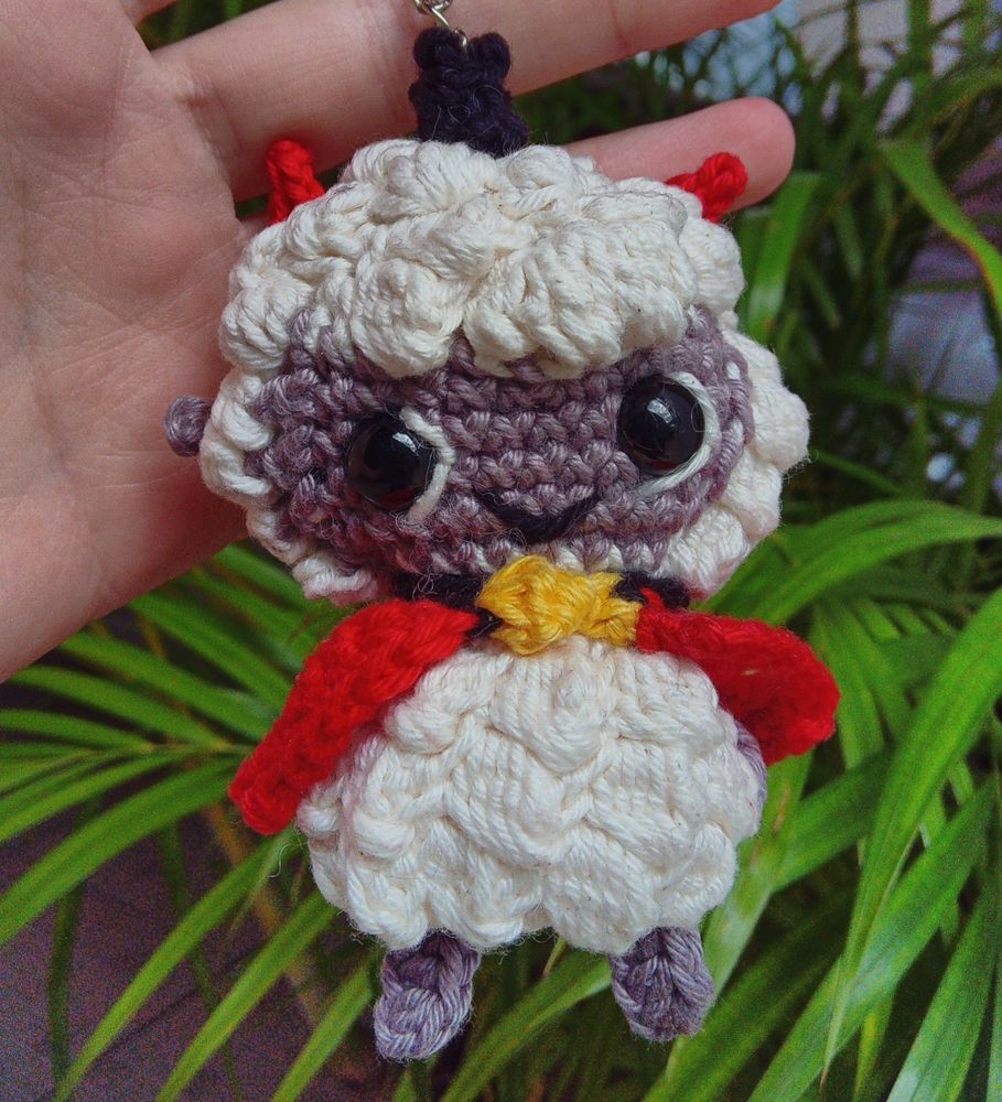 Chaveiro do Cordeiro protagonista do jogo Cult Of The Lamb com seu olhar pro ladinho, sua capa vermelha com sininho, com seus chifres e coroa preta 
