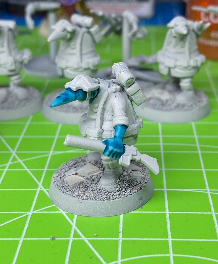 Another grey primed WIP Quar Crusader with turquoise freckled skin holding a Bogen rifle. Standing on a bright green cutting board.