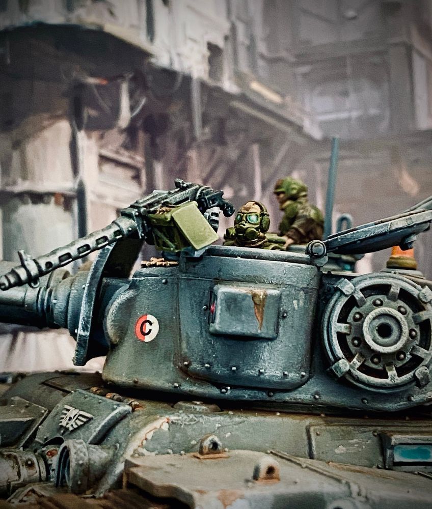Crew member of the same tank wearing a gas mask and goggles having a look from another turret hatch with a pintle mounted heavy stubber