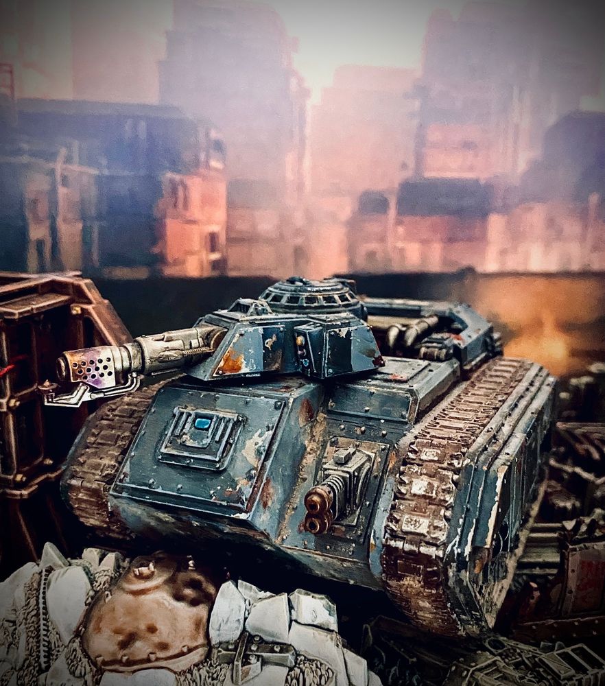 Battered up Hellhound Flamethrower Tank in grey/dark grey camo with lots of chipping and rust. Set in a ruin scene partially lit by flames. From front slightly left.