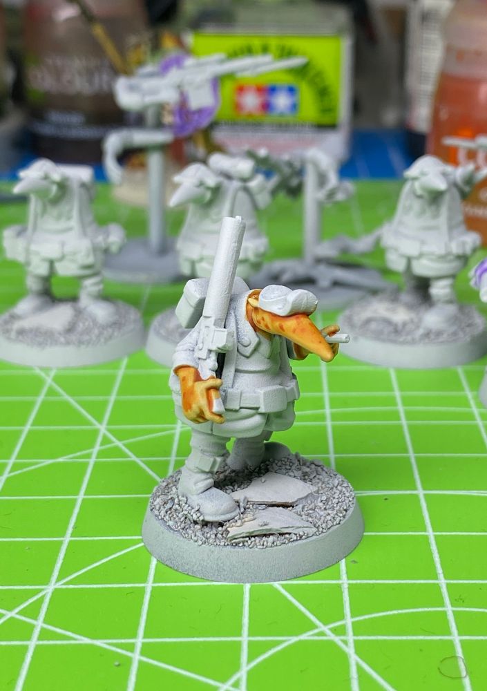 Grey primed WIP Quar Crusader with bright orange skin holding a Bogen rifle. Standing on a bright green cutting board.