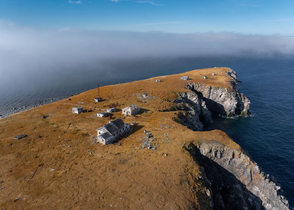 An aerial view of a cluster of small abandoned buildings on a treeless island with a steep cliff shoreline (Vadim Makhorov / AP)