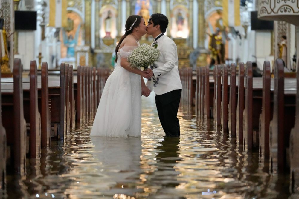 A newlywed couple kisses after a wedding ceremony inside a church that has been flooded, with about a foot of standing floodwater. (Aaron Favila / AP)