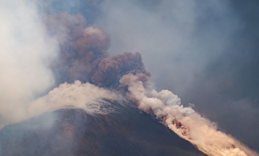 A plume of ash rises from a volcano, with steaming pumice surrounding its crater. (Marco Restivo / Reuters)