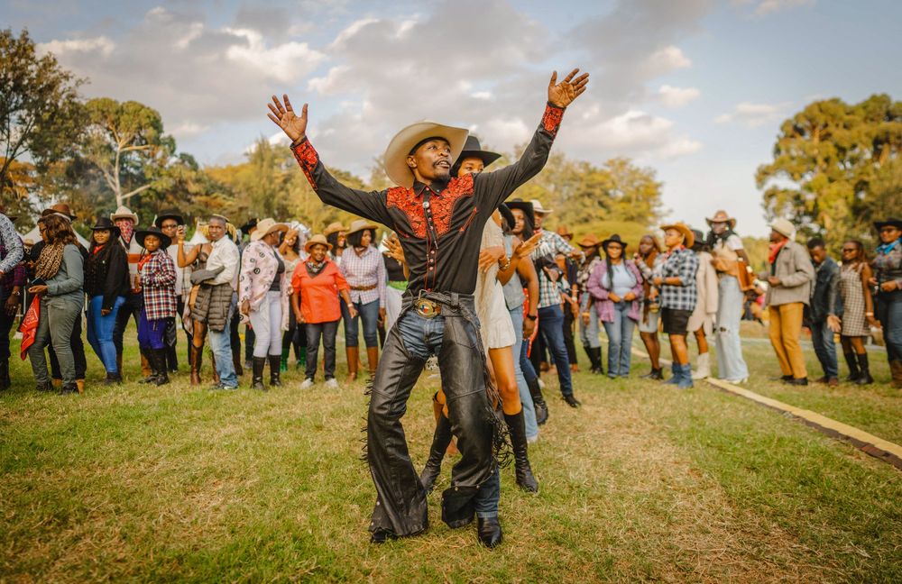 A man wearing chaps and a cowboy hat leads a line of dancing people at an outdoor country music festival in Kenya. (Fredrik Lerneryd / AFP / Getty)