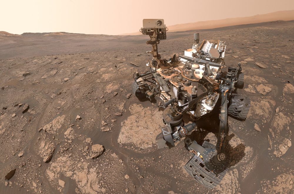 A selfie of a large Mars rover, with a reddish-colored dry, rocky, and dusty Martian landscape in the background. (JPL / NASA)