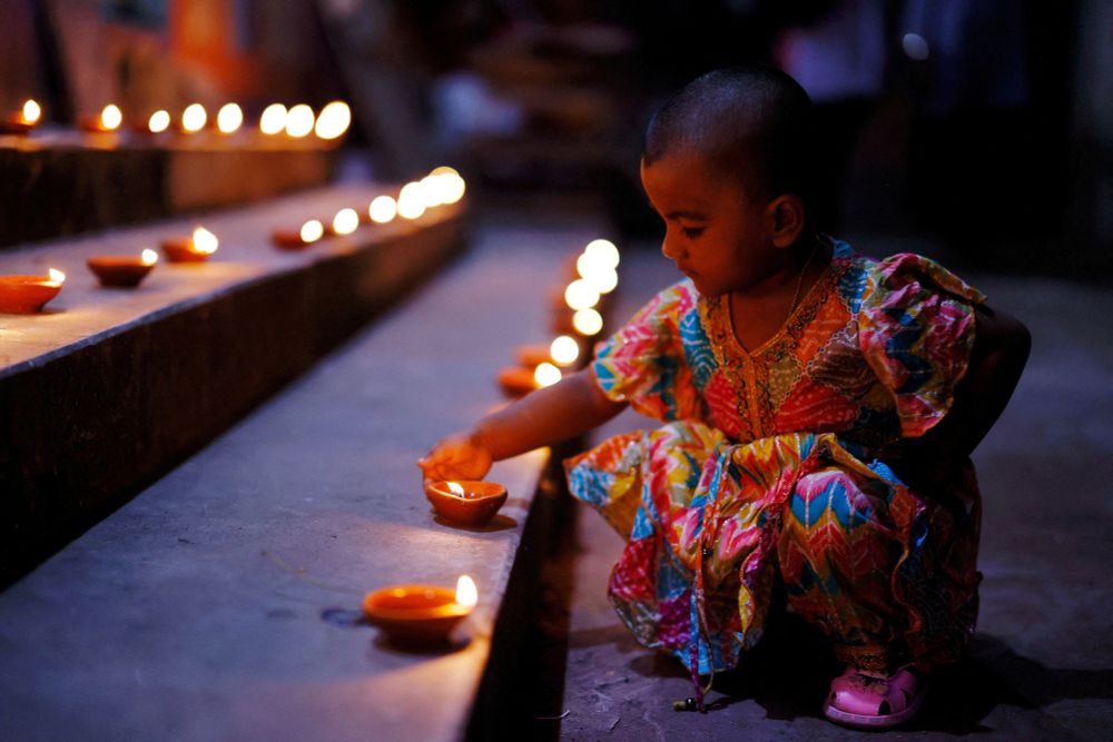 A child kneels down to touch one of many small oil lamps laid out on temple steps. (Mohammad Ponir Hossain / Reuters)