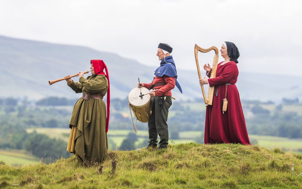 A trio of musicians wearing medieval clothing performs on a hilltop. (Danny Lawson / PA Images / Getty)