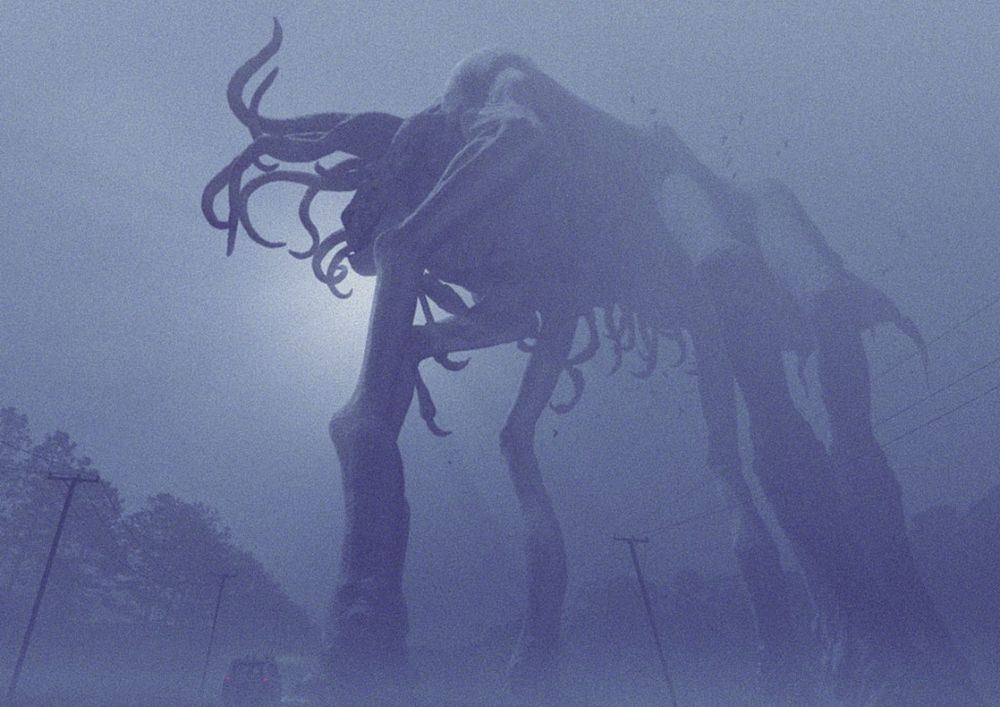A giant movie monster, seen in mist, with six long legs, a long body, and many tentacles and hooked appendages.