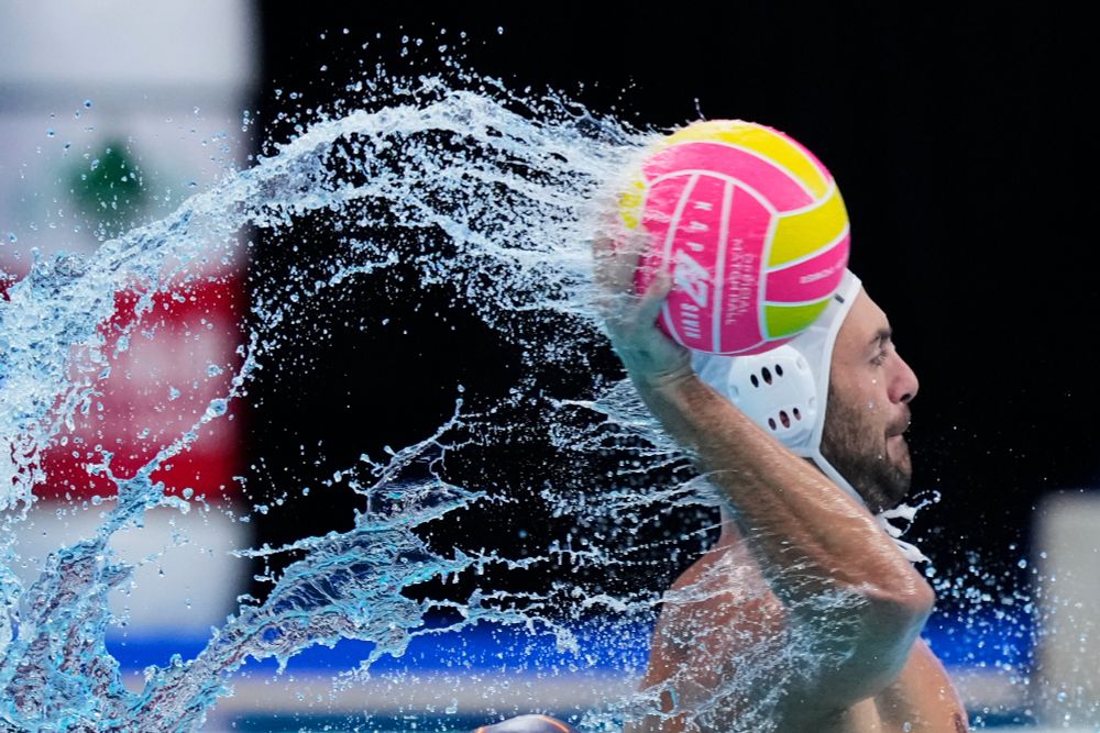 A water polo player throws a ball, splashing pool water all over the place. (Vincent Thian / AP)