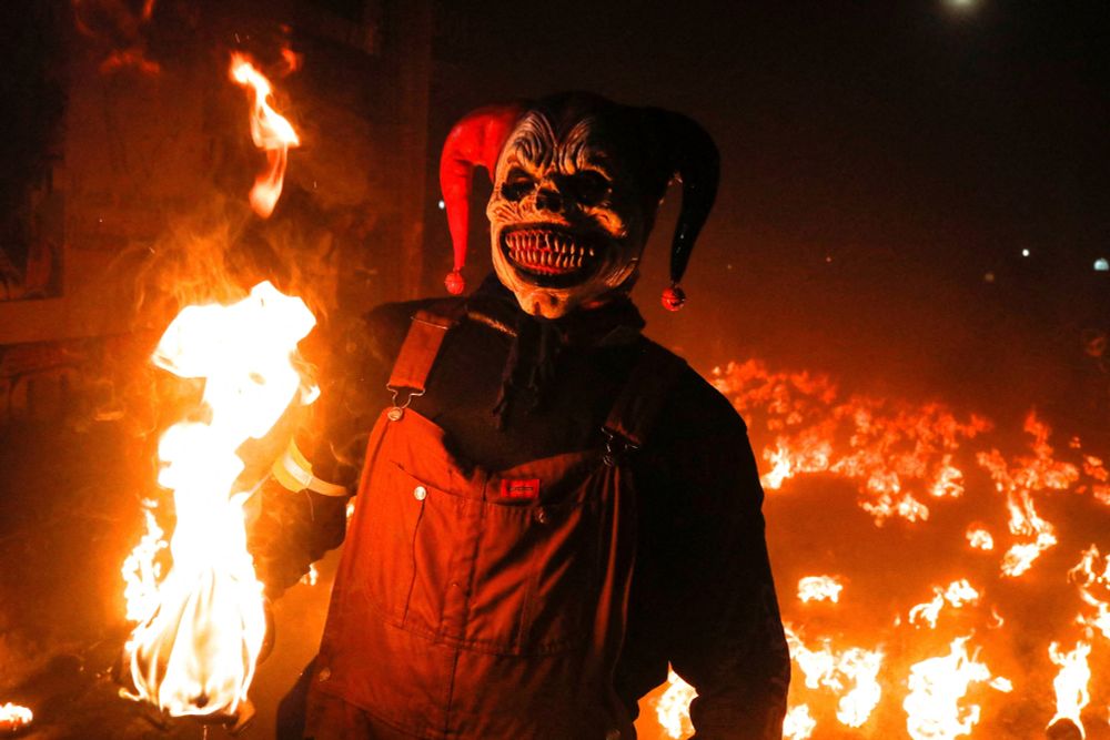 A person wearing a frightening clown mask poses in front of a fiery background. (Jose Cabezas / Reuters)