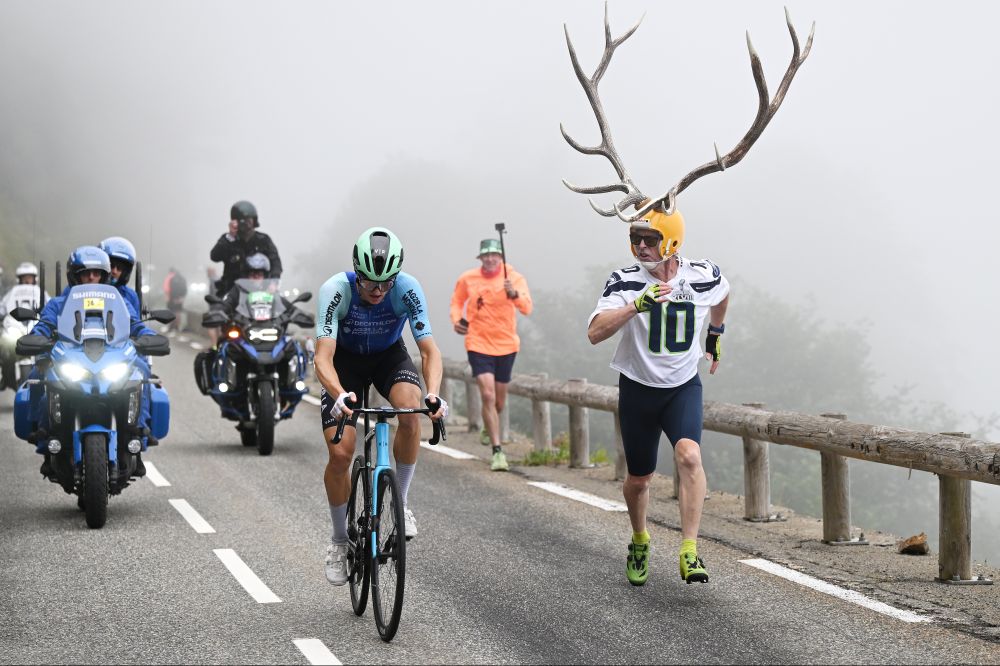 A fan wearing a helmet adorned with gigantic antlers runs beside a cyclist during the Tour de France. (Tim de Waele / Getty)