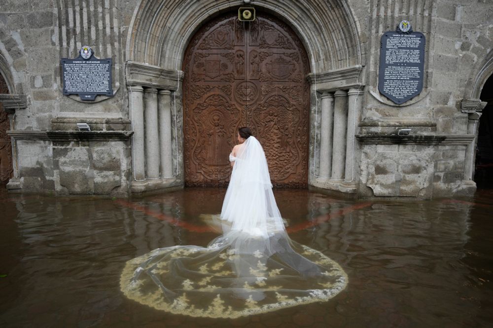 A bride with a long, flowing train, stands in foot-deep floodwater outside a church. (Aaron Favila / AP)