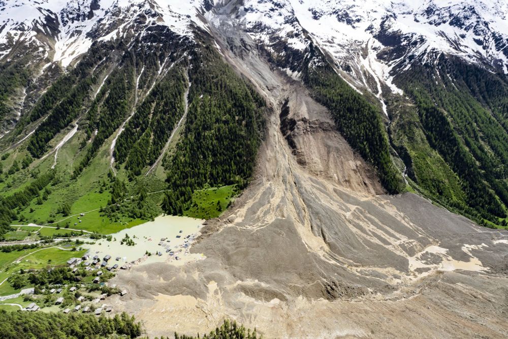 An aerial view of the side of a mountain valley, scarred by a recent landslide, covering much of a village below. (Jean-Christophe Bott / Keystone / AP)
