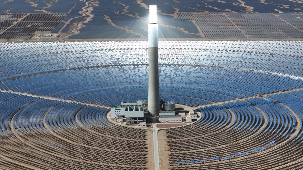 An aerial view of a solar thermal plant—a tall cylindrical column being illuminated by sunlight reflected from a huge array of large mirrors arranged in concentric circles around its base (Ma Mingyan / China News Service / VCG / Getty)