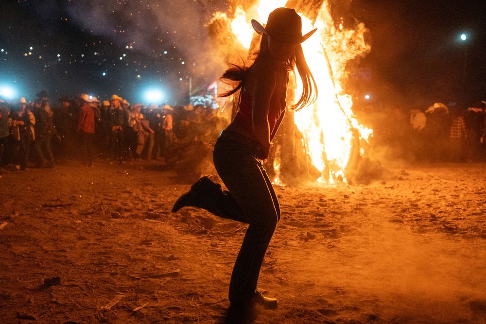 A woman wearing a cowboy hat dances in front of a bonfire. (Guillermo Arias / AFP / Getty)
