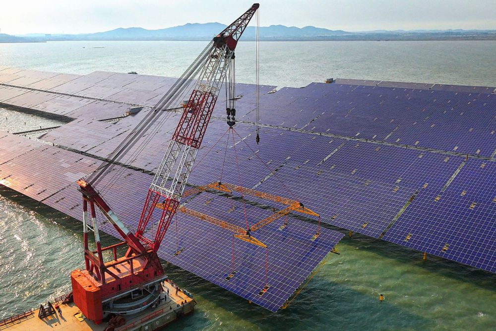 A crane on a floating barge positions a large solar panel for installation. (AFP / Getty)