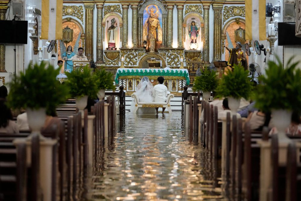 A couple sits together on a small bench during a wedding ceremony in a flooded church. (Aaron Favila / AP)