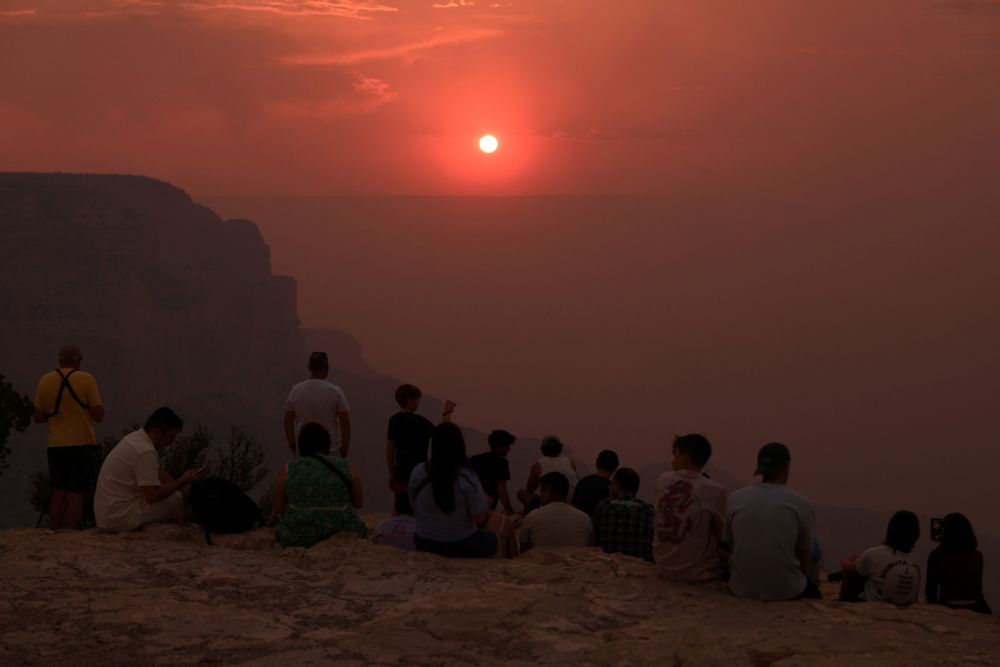 Visitors on the rim of the Grand Canyon watch a deep red sunset through a haze of wildfire smoke. (David Swanson / Reuters)