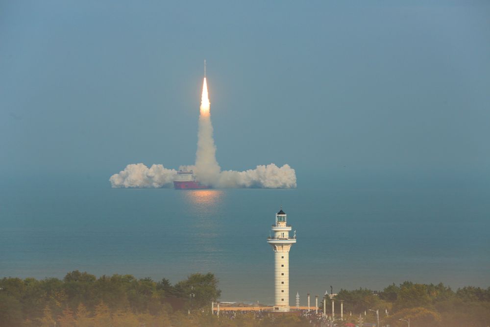 A rocket lifts off from the deck of a ship, seen from a distance with a lighthouse in the foreground. (Zheng Peibo / VCG / Getty)