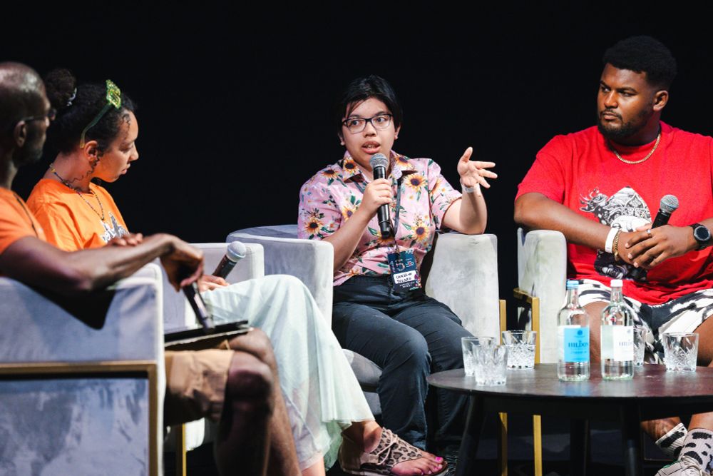 Cameryn Tuliao in a pink button up with sunflowers, talking at a panel. This picture was taken at BAFTA YGD Showcase 2025, photographed by ©BAFTA/Alecsandra Dragoi