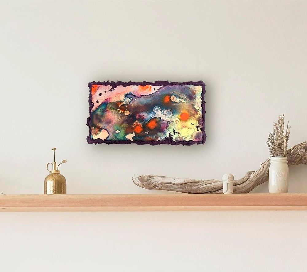 Colorful abstract painting on a beige wall above a wood shelf. The painting features fluid organic shapes in dark purple, orange, and teal on an iridescent luminous panel. The artwork format is horizontal and the edges of the panel are covered in highly textured thick purple paint which forms an intriguing frame. The shelf below is holding a few neutral objects such as a brass oil can, a vase of lavender, and driftwood.