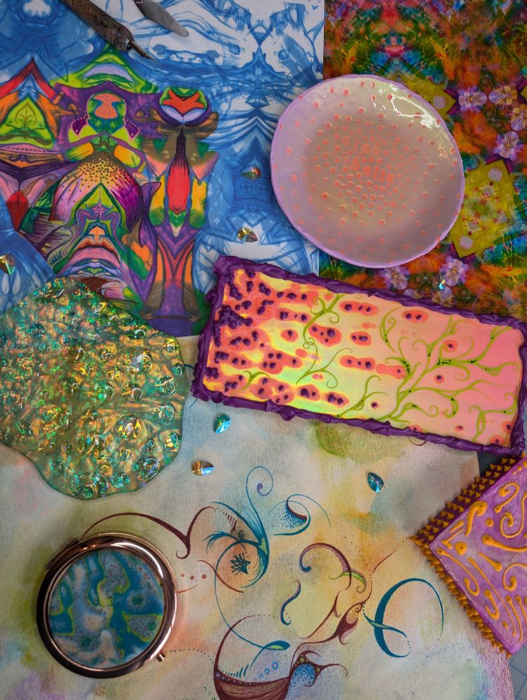Overhead image of very bright colorful handmade crafts and art, blue decorated compact mirror on the lower left, iridescent blue coaster middle left, small reflective abstract pink art in the middle. There is a pastel purple polymer clay trinket dish towards the top and the background images are colorful abstract patterns that were made with mixed media including pens, paint, and a printer 