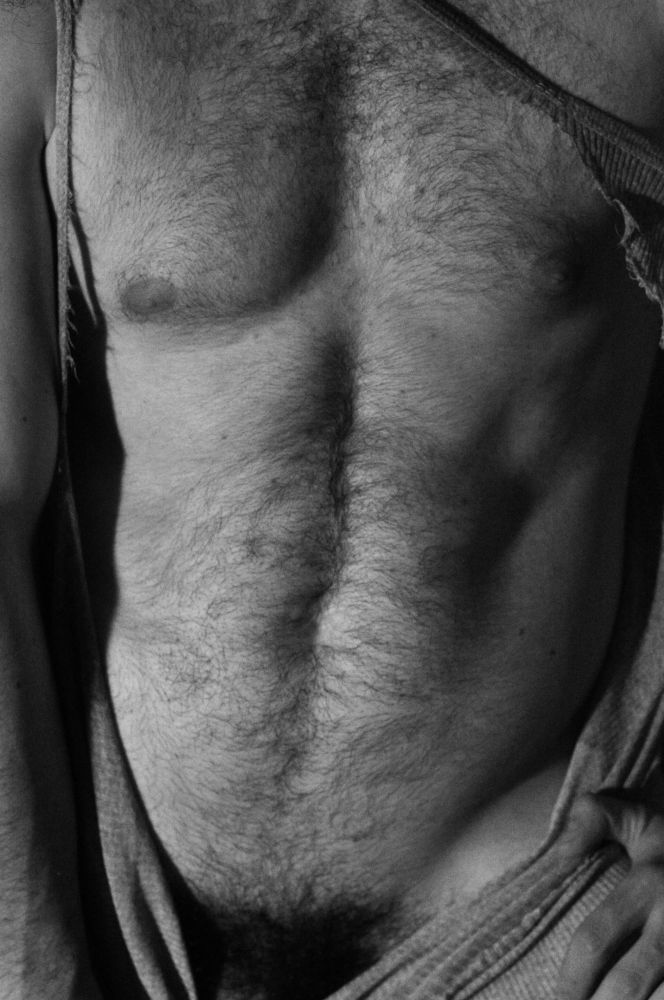 Bauhaus wearing a heavily ripped tank top exposing their torso and bush