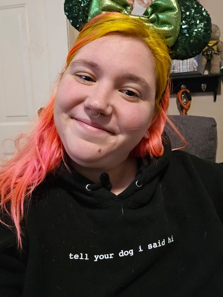 Happy woman smiling wearing green minnie mouse ears and a sweatshirt that says "tell your dog I said hi" 