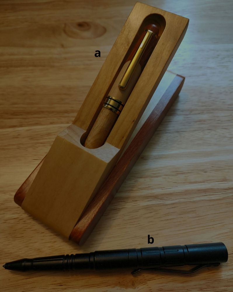 a) a wooden pen and case. b) a black steel pen. Both are on a wooden background.