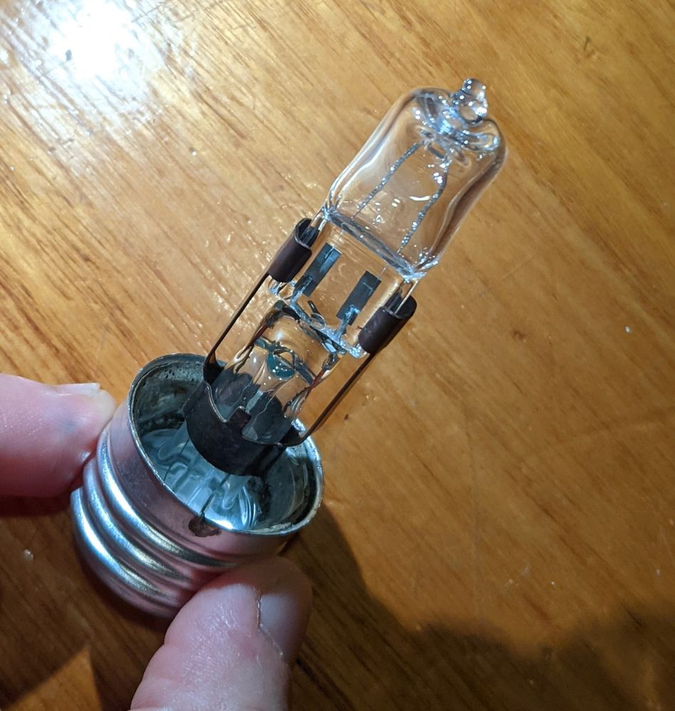 an LED globe connected to the inner stand of a screw globe using a copper clip. the bayonets of the LED are twisted into the powered wires of the screw globe. the screw part of the old globe is held in someone's hand