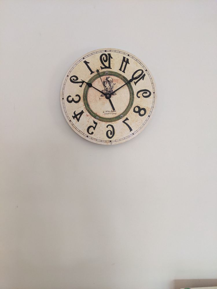 a cream-coloured circular wall clock that's a mirror image of normal clocks, with a picture of the mad hatter on it 