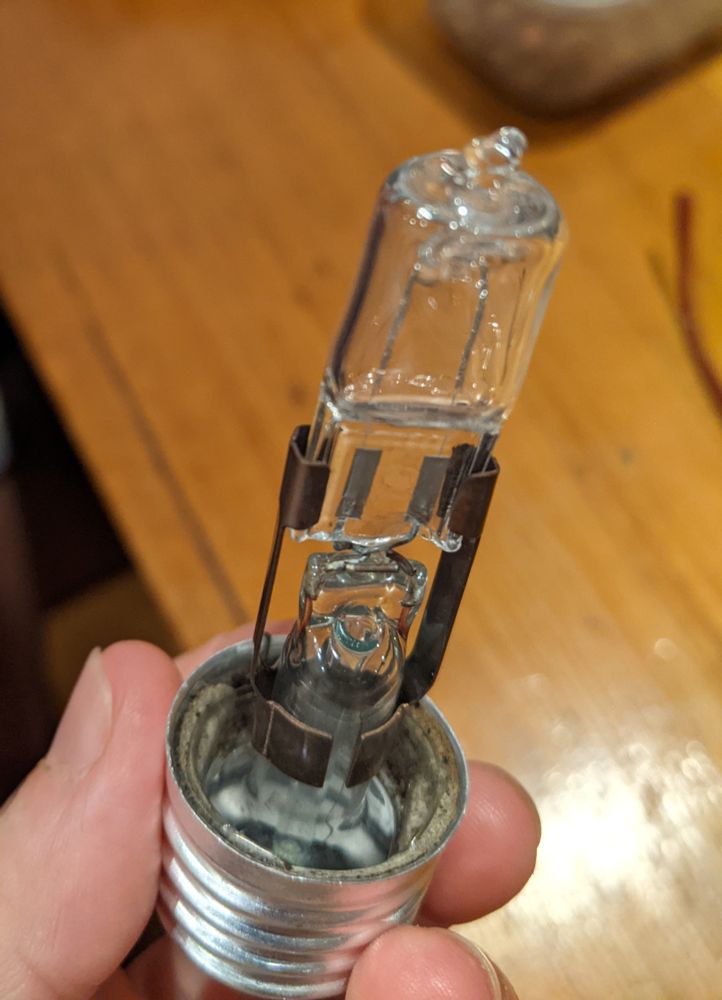 an LED globe connected to the inner stand of a screw globe using a copper clip. the bayonets of the LED are twisted into the powered wires of the screw globe. the screw part of the old globe is held in someone's hand