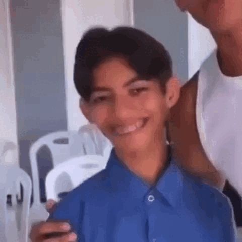 a young boy in a blue shirt is smiling for the camera while standing next to a man in a white tank top .