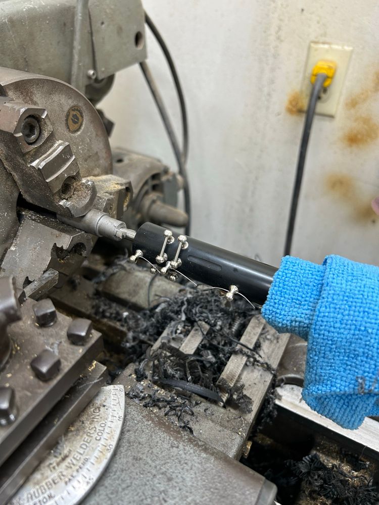 Large machinist lathe with a boring bit and centering guide. A plastic oboe upper joint is being prepped to have a broken tenon bored out for replacement.