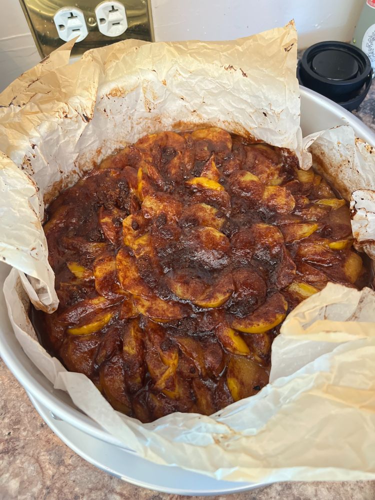 A cake in a pan lined with parchment paper. It is topped with a LOT of plums, and a brown sugar & butter mixture.