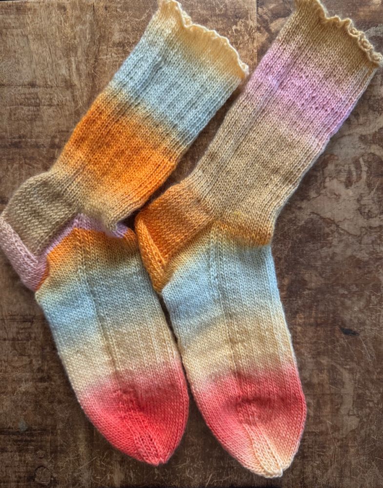 Hand knit socks in shades of sunset on a wood background. 