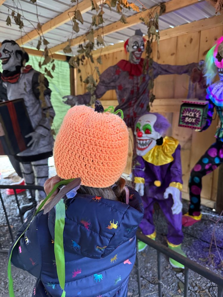 A young child wearing a pumpkin hat and navy coat from behind looking at a Halloween display of clowns.