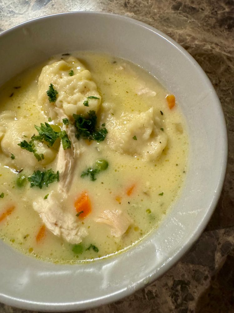 Chicken and dumpling in a grey bowl on a brown faux marble countertop. 