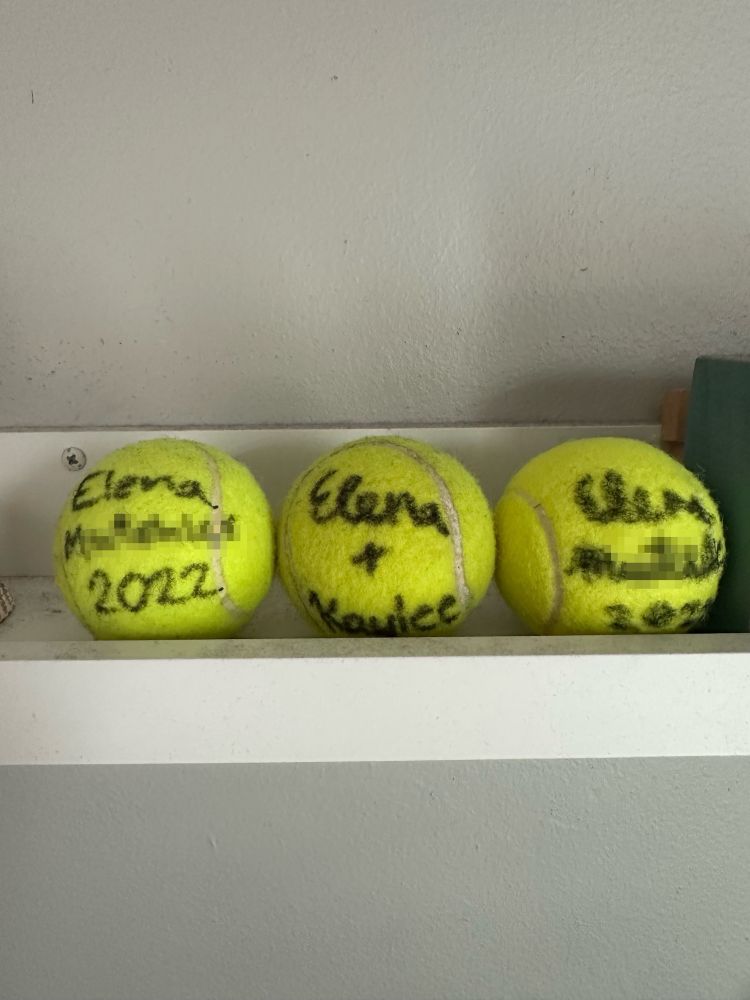 Three tennis balls signed by Elena sitting on a shelf. 