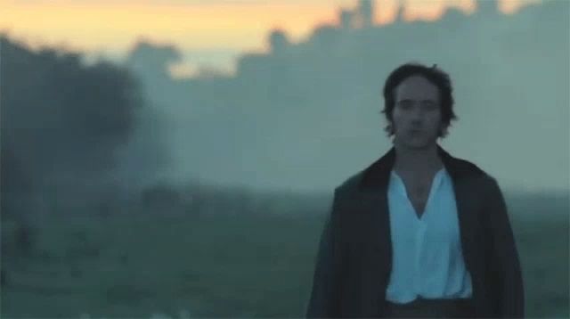 a man in a white shirt and black jacket is walking in a field .