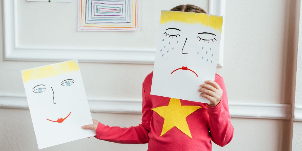 Et barn holder opp to tegninger foran ansiktet en med smilefjes en med trist fjes. Bilde fra colourbox.com