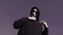 a man in a black hoodie with a skeleton on his shirt is standing in front of a purple background .